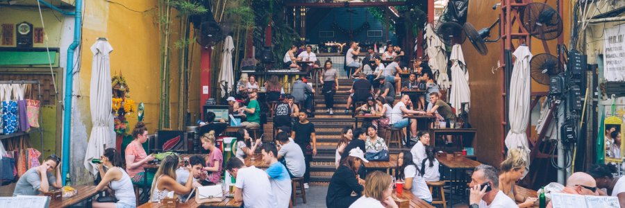 Photo shows groups of people sat around tables at a street bar.